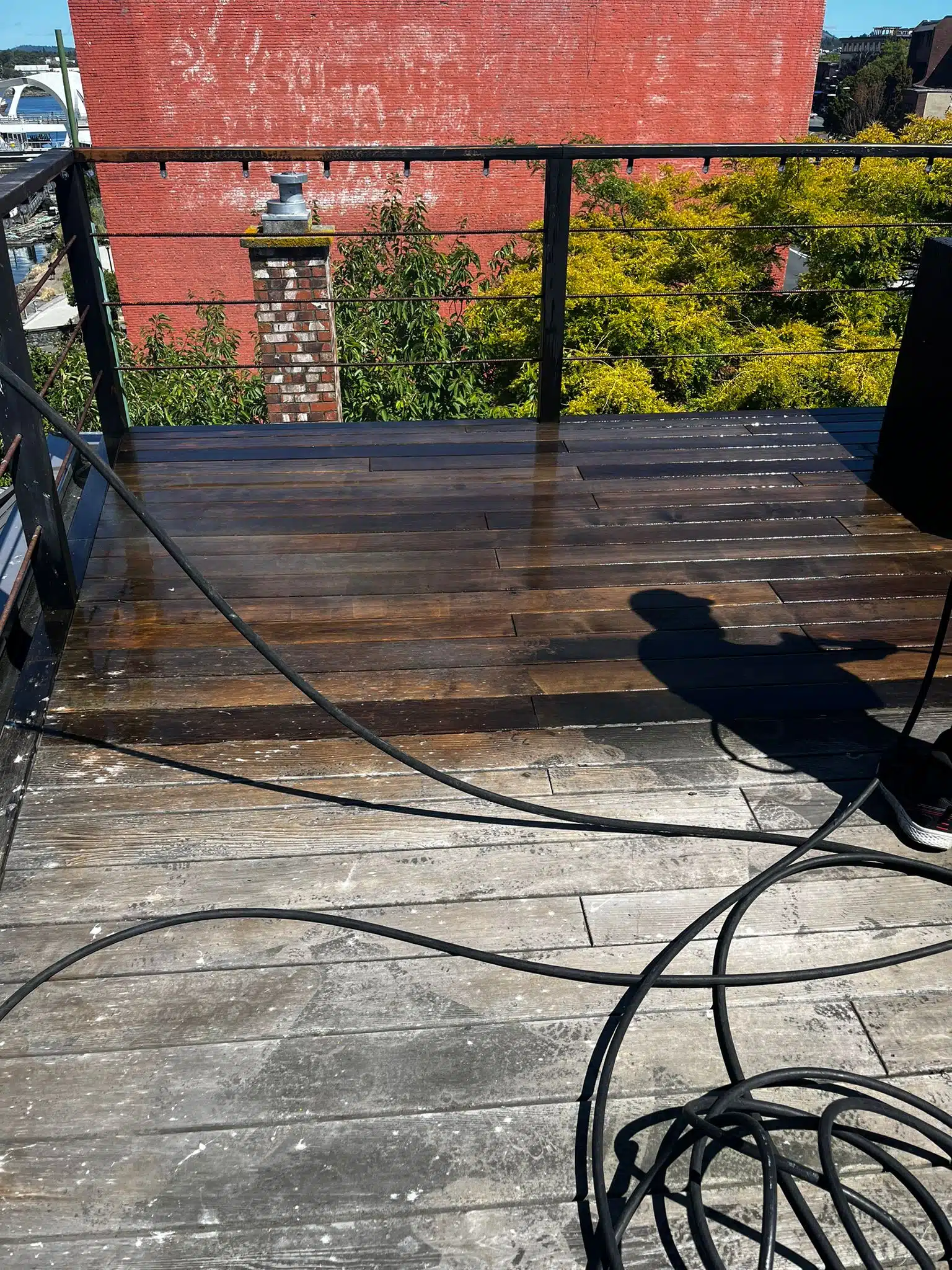 Side-by-side comparison of a wood deck before and after professional pressure washing by Titus Brothers. The bottom side shows dirt, grime, bird fecal matter, and mildew buildup, while the top side reveals a clean, bright wooden surface after pressure washing.